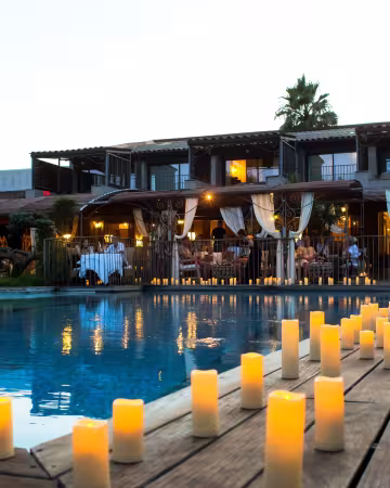 Piscine de l'hôtel à la tombée de la nuit, bordée de bougies allumées, devant le restaurant éclairé