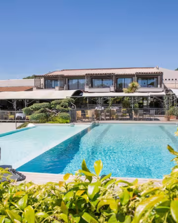 Piscine de l'hôtel Le Roi Théodore entourée de jardins, avec les bâtiments de l'hôtel au fond
